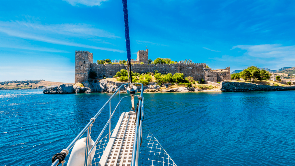 Bodrum yat kiralama turu sırasında turkuaz sulara demirlemiş lüks bir gulet ve arka planda tarihi Aziz Petrus Kalesi.