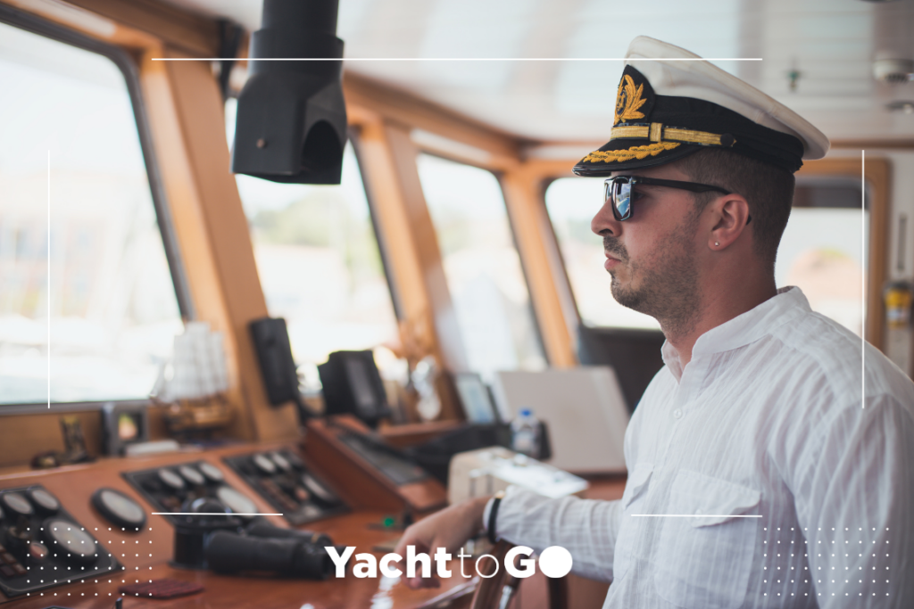 Un capitán de yate de pie en el timón comprobando la previsión de viento meltemi en una pantalla digital.