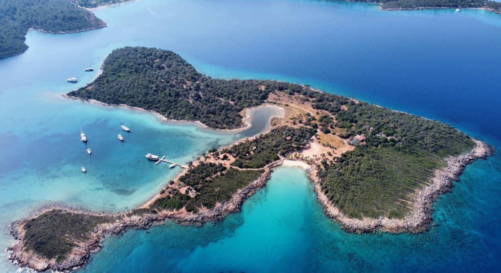 Η διάσημη χρυσή άμμος της παραλίας Κλεοπάτρα στο νησί Σεντίρ, με κρυστάλλινα ρηχά νερά και αρχαία ερείπια στο βάθος.
