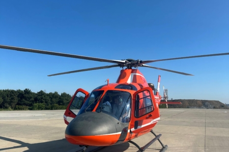A silver agusta 119 koala private helicopter parked at a coastal helipad ready for charter.