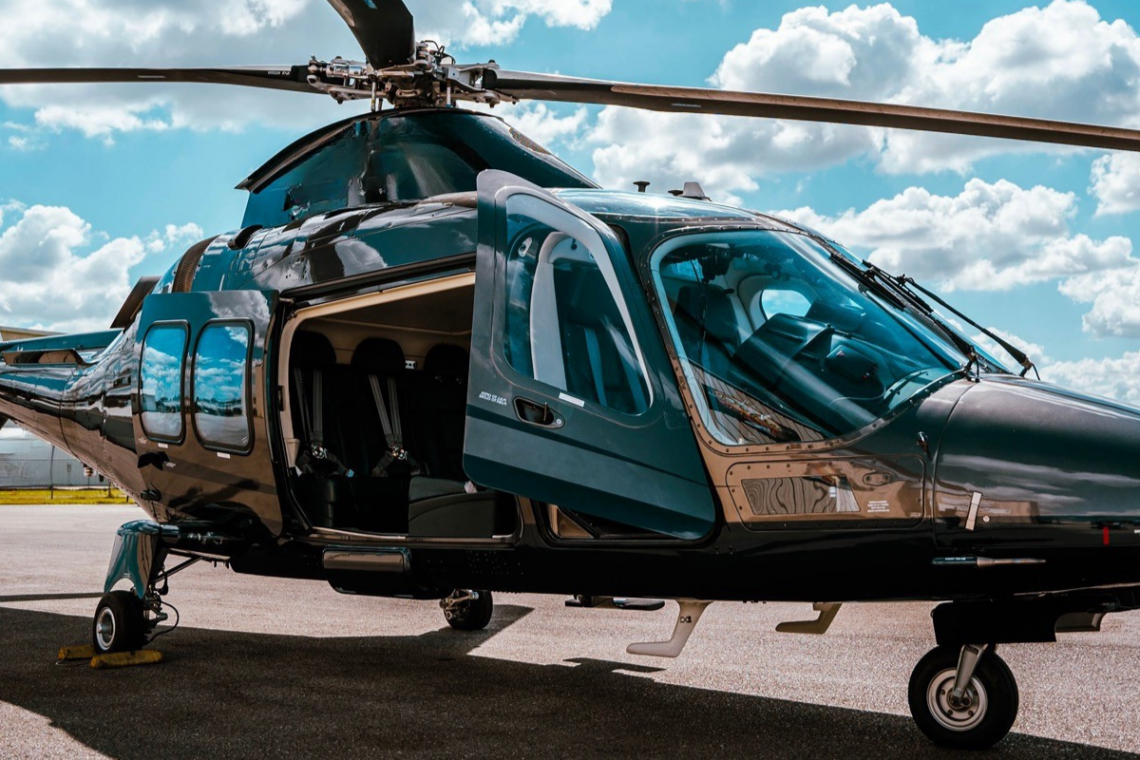 A VIP twin-engine helicopter flying over the turquoise waters of Costa Smeralda, approaching a superyacht in Porto Cervo.