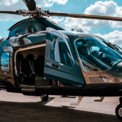 A VIP twin-engine helicopter flying over the turquoise waters of Costa Smeralda, approaching a superyacht in Porto Cervo.